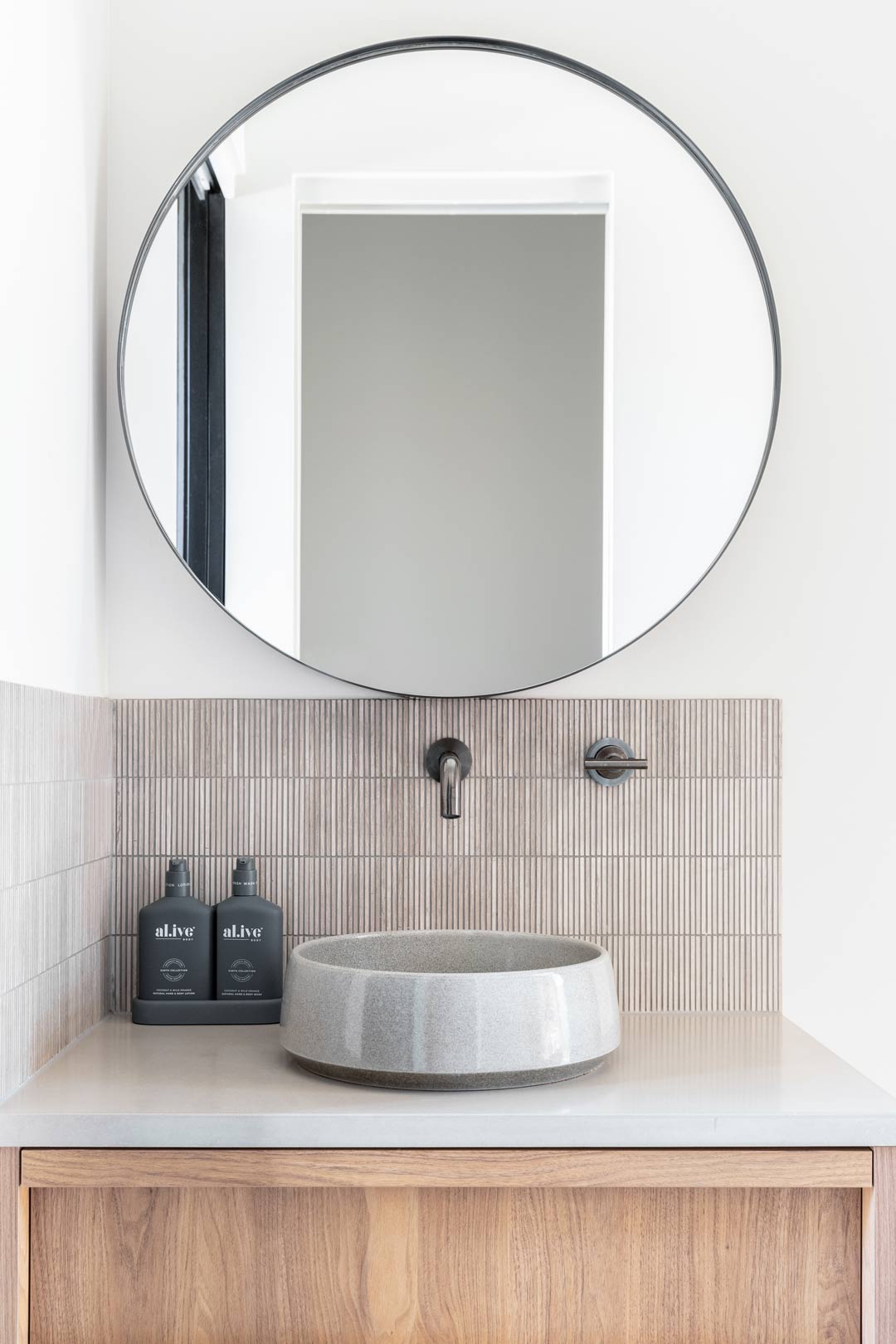A-coastal-powder-room-with-travertine-slither-feature-tiles-a-ceramic-round-basin-and-brushed-gunmetal-tapware