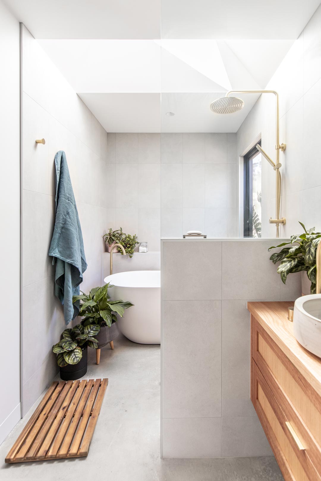 A-concrete-look-bathroom-with-a-concrete-bathroom-floor-paired-with-concrete-look-tiles-is-warmed-by-a-natural-timber-vanity-and-green-indoor-plants