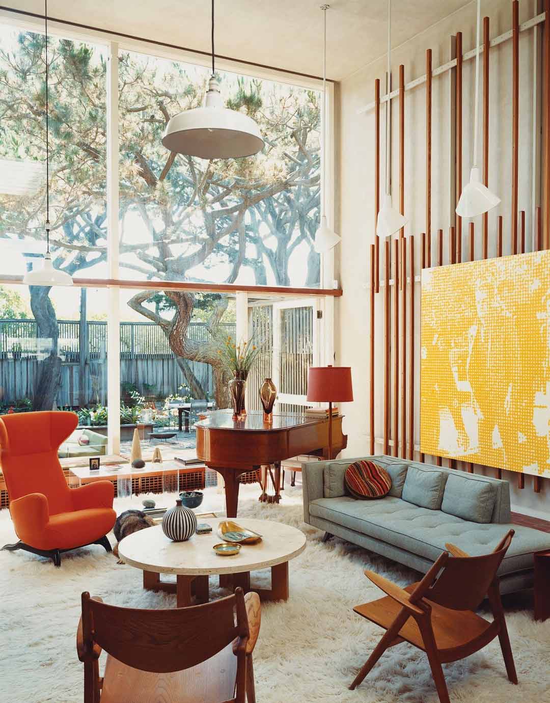 A-light-and-spacious-mid-century-open-plan-living-room-with-an-orange-accent-chair-bold-yellow-artwork-and-timber-furniture