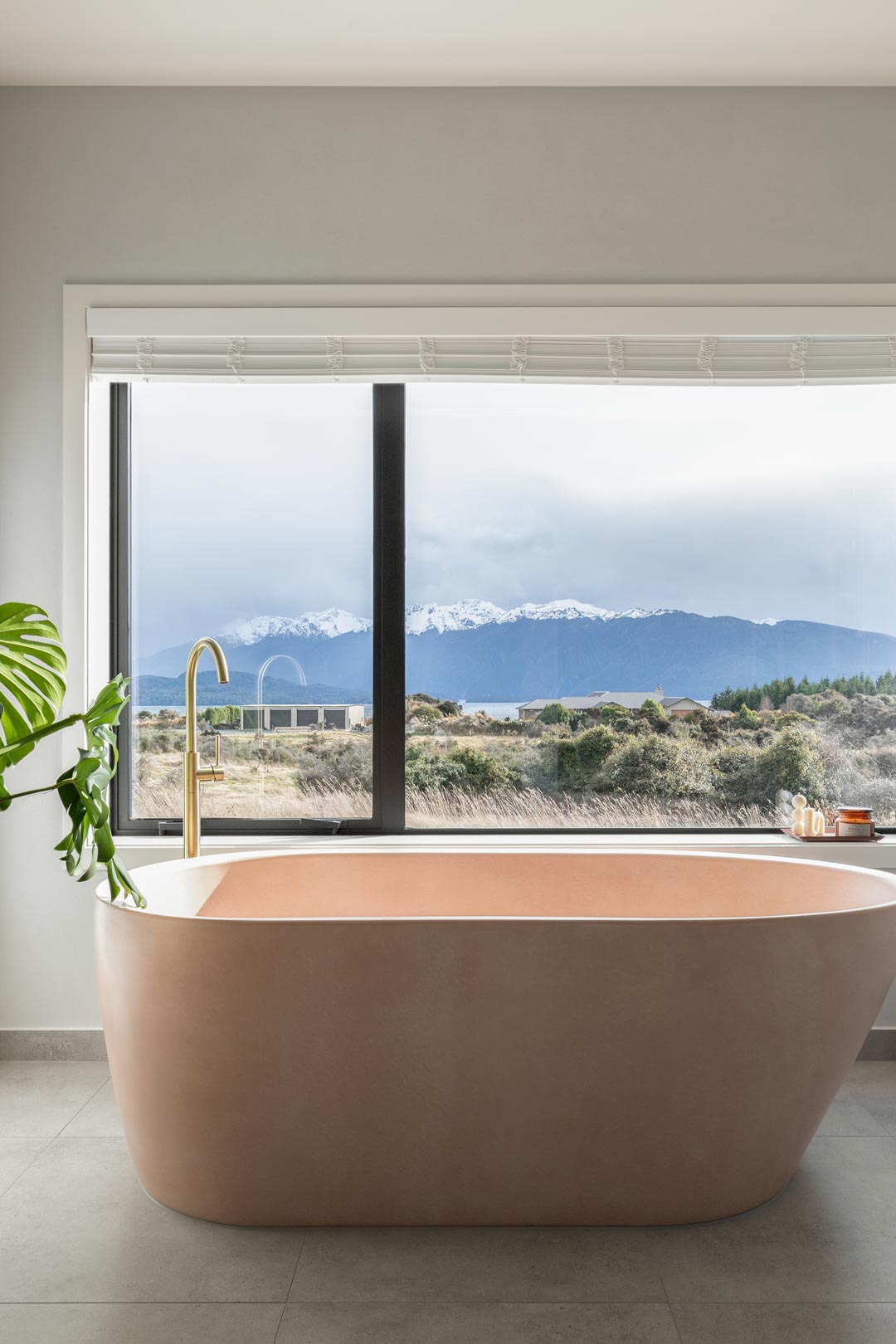 A-luxurious-pink-concrete-bath-with-brushed-brass-tap-sits-in-front-of-a-window-overlooking-the-mountains-of-New-Zealand