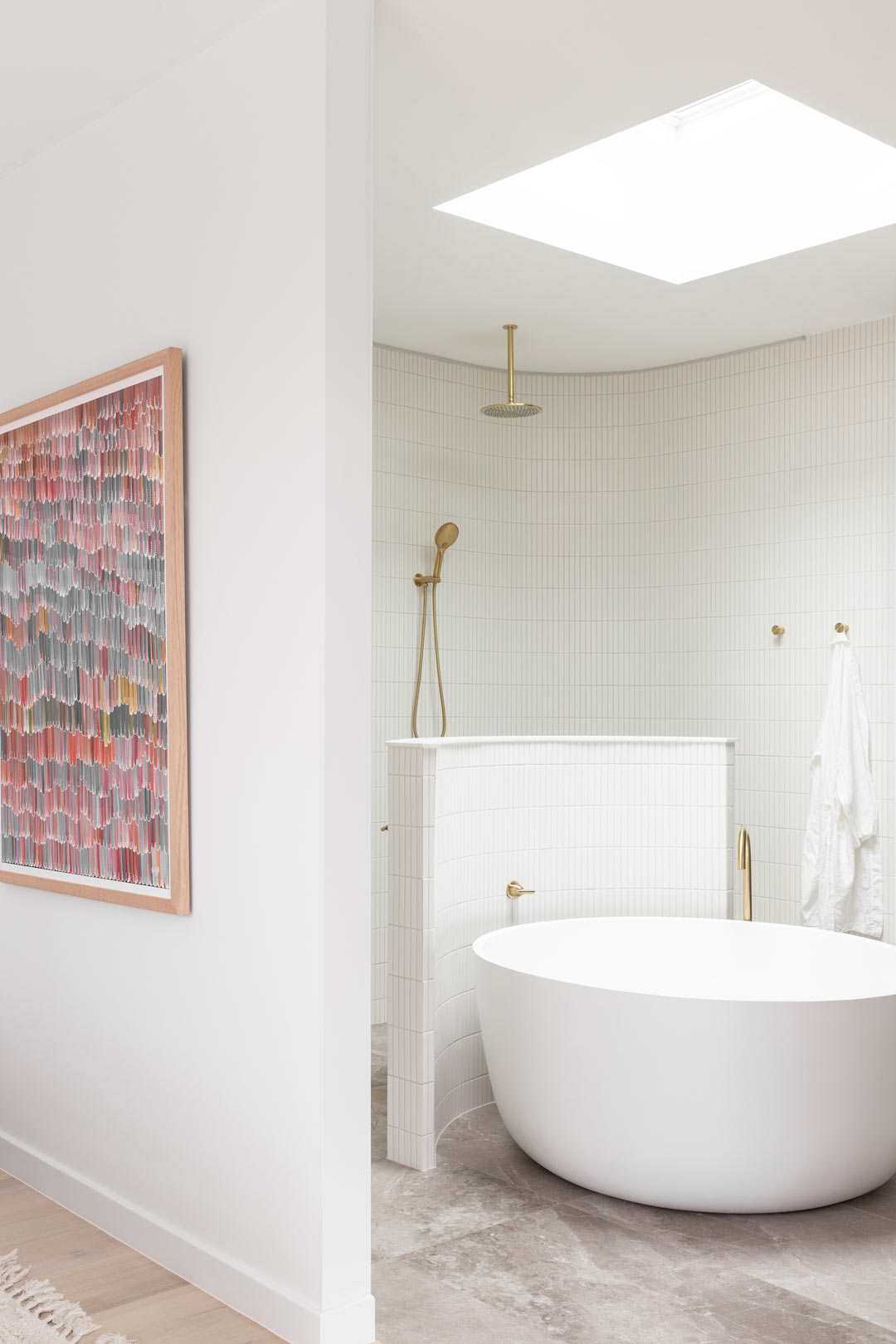 A-luxury-master-bedroom-with-a-muted-pastel-colour-palette-meets-an-open-ensuite-with-brushed-brass-tapware-and-a-circular-bath