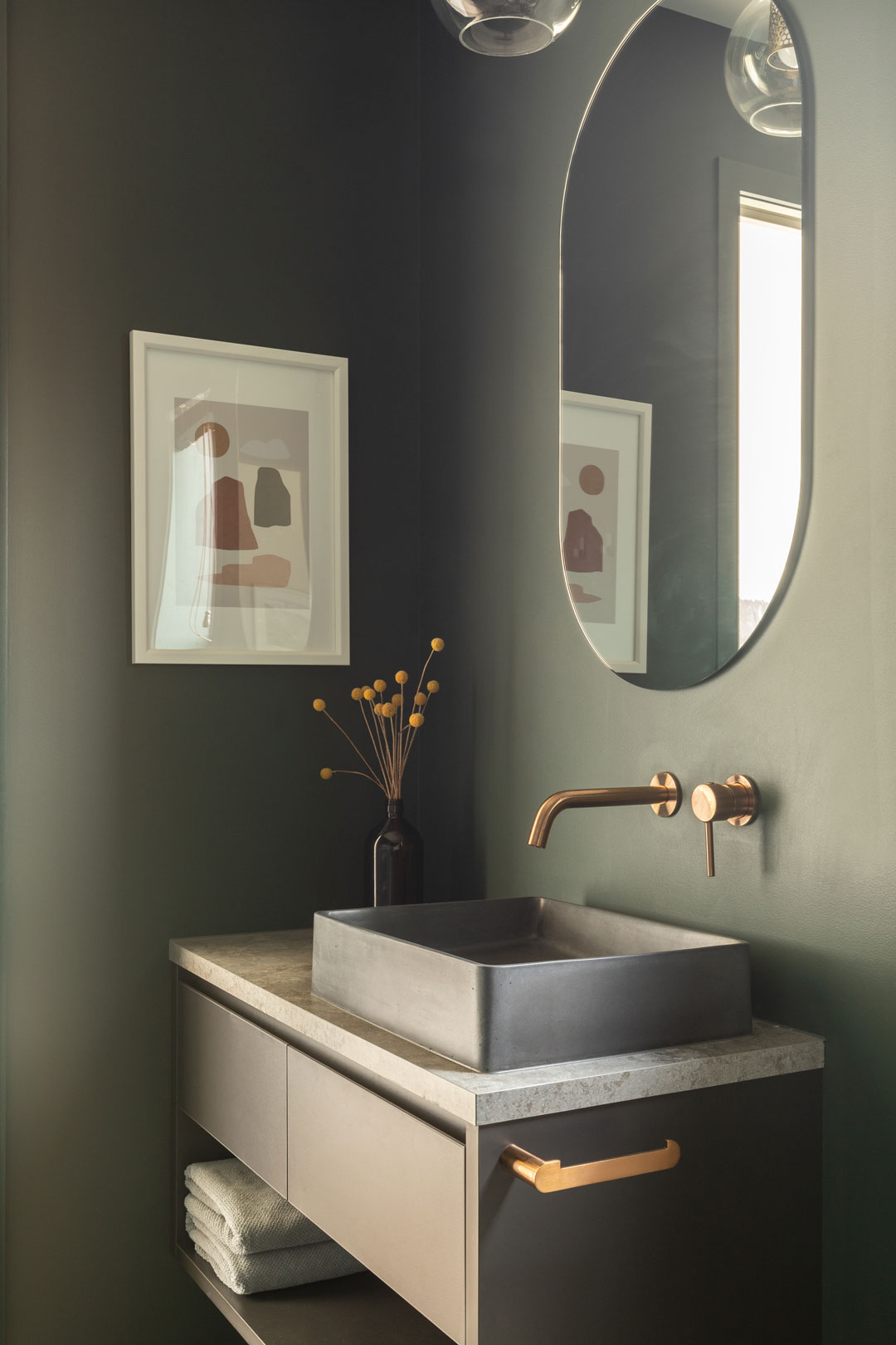 A-muted-green-bathroom-with-a-concrete-basin-and-brushed-brass-tapware