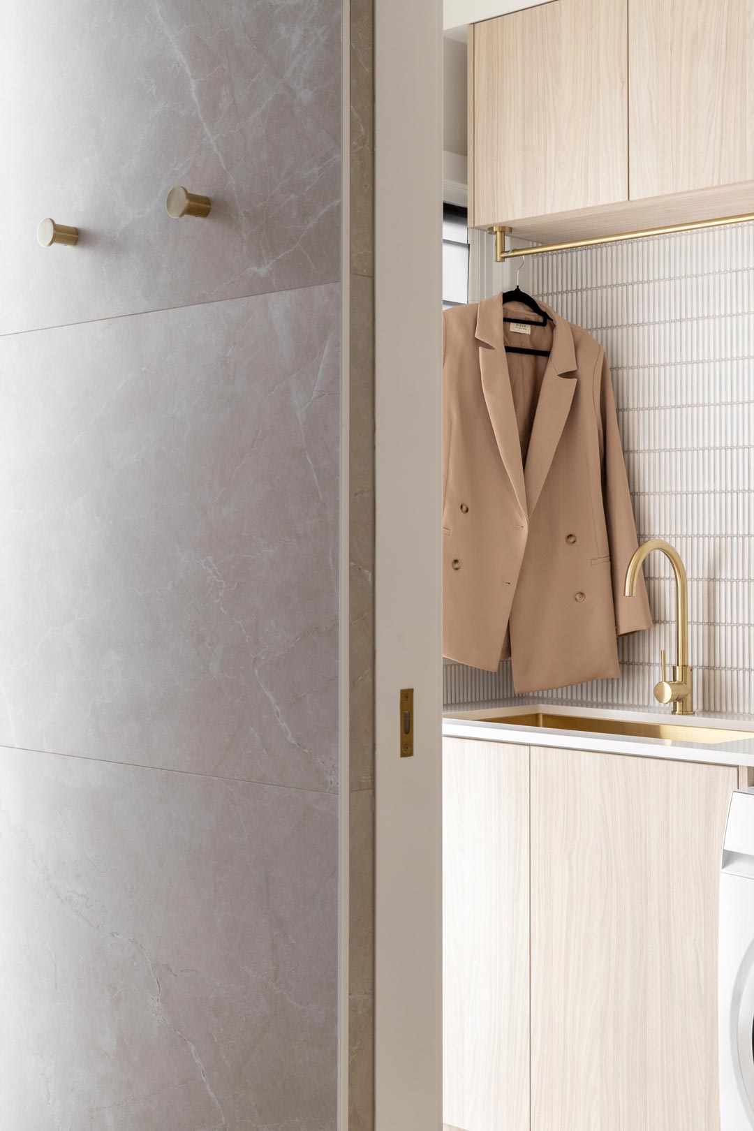 A-simple-elegant-neutral-laundry-with-light-timber-cabinetry-brushed-brass-tapware-and-clothes-hanging-rail
