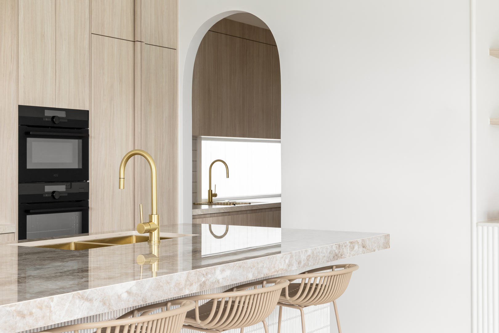 A-warm-kitchen-with-brushed-brass-tapware-soft-timber-cabinetry-and-a-stunning-natural-stone-bench-top-opens-up-to-a-butlers-pantry