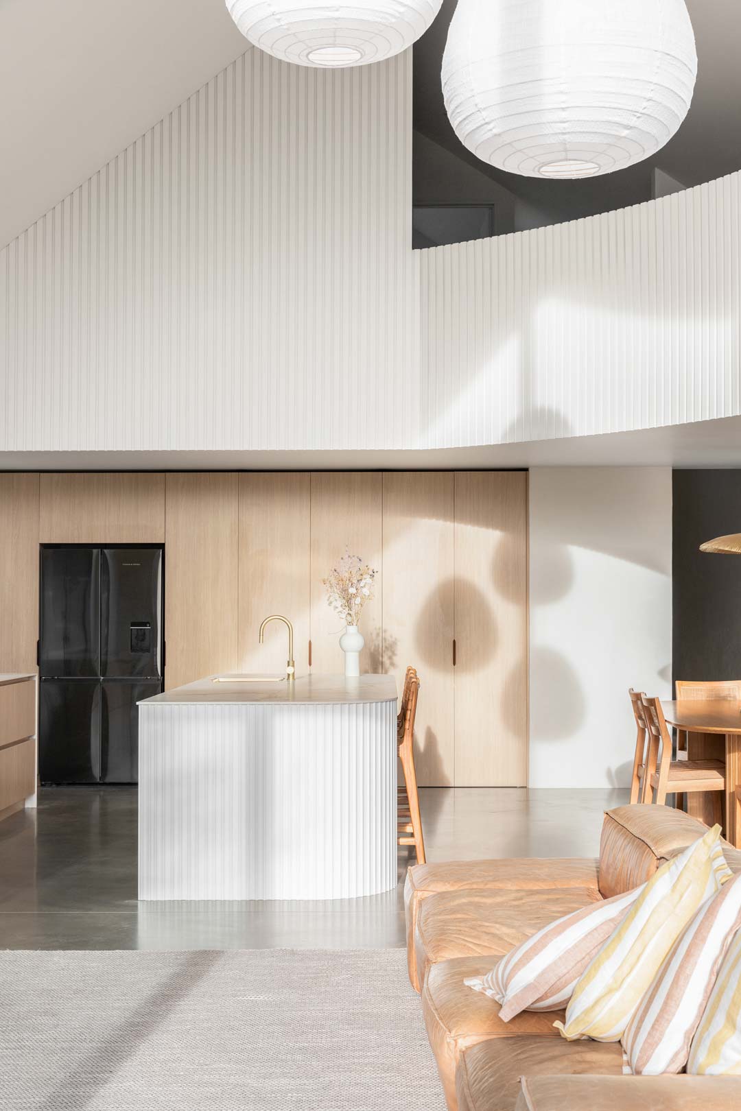 A-warm-open-kitchen-in-a-barn-style-house-with-a-soft-leather-couch-timber-cabinetry-and-a-large-island-bench