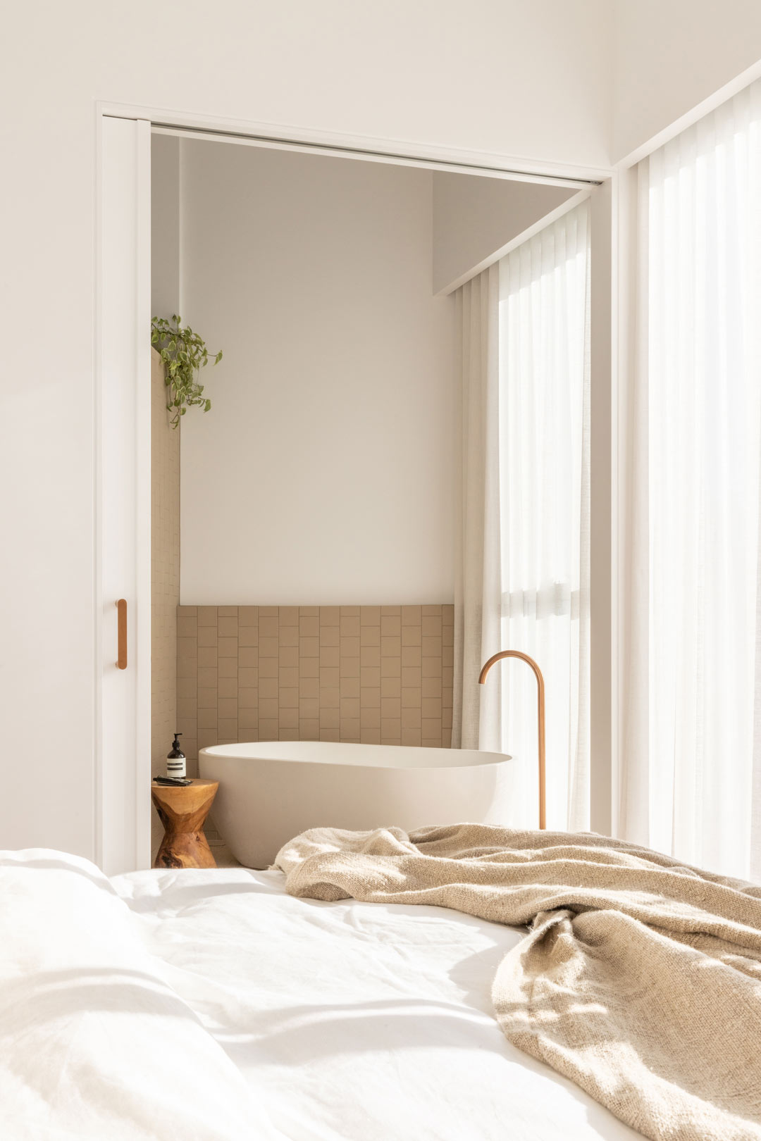 A-warm-toned-master-bedroom-and-ensuite-of-a-mordern-coastal-home-with-brushed-copper-bath-filler-and-soft-sheer-curtains.jpg?format=webp&width=1040