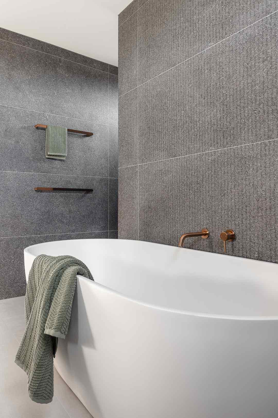 An-industrial-style-bathroom-with-grey-textured-tiles-green-towels-and-brushed-copper-tapware