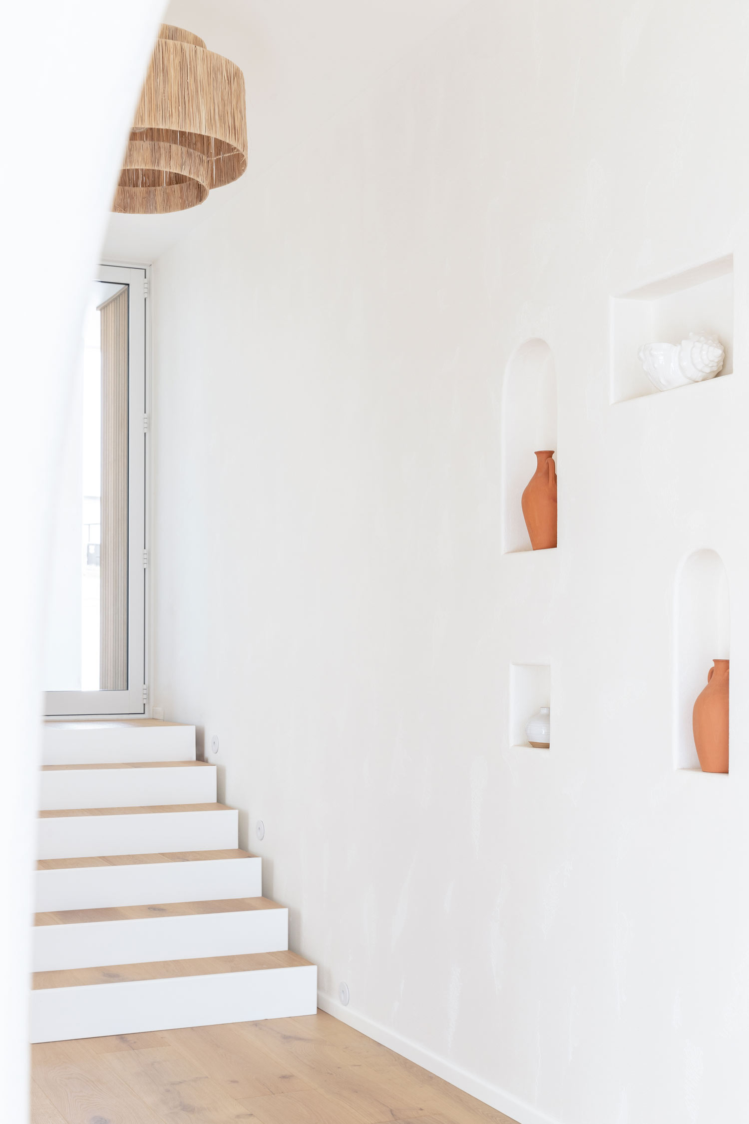 Hallway-in-a-modern-mediterranean-house-with-light-timber-floors-woven-pendent-and-niche-wall