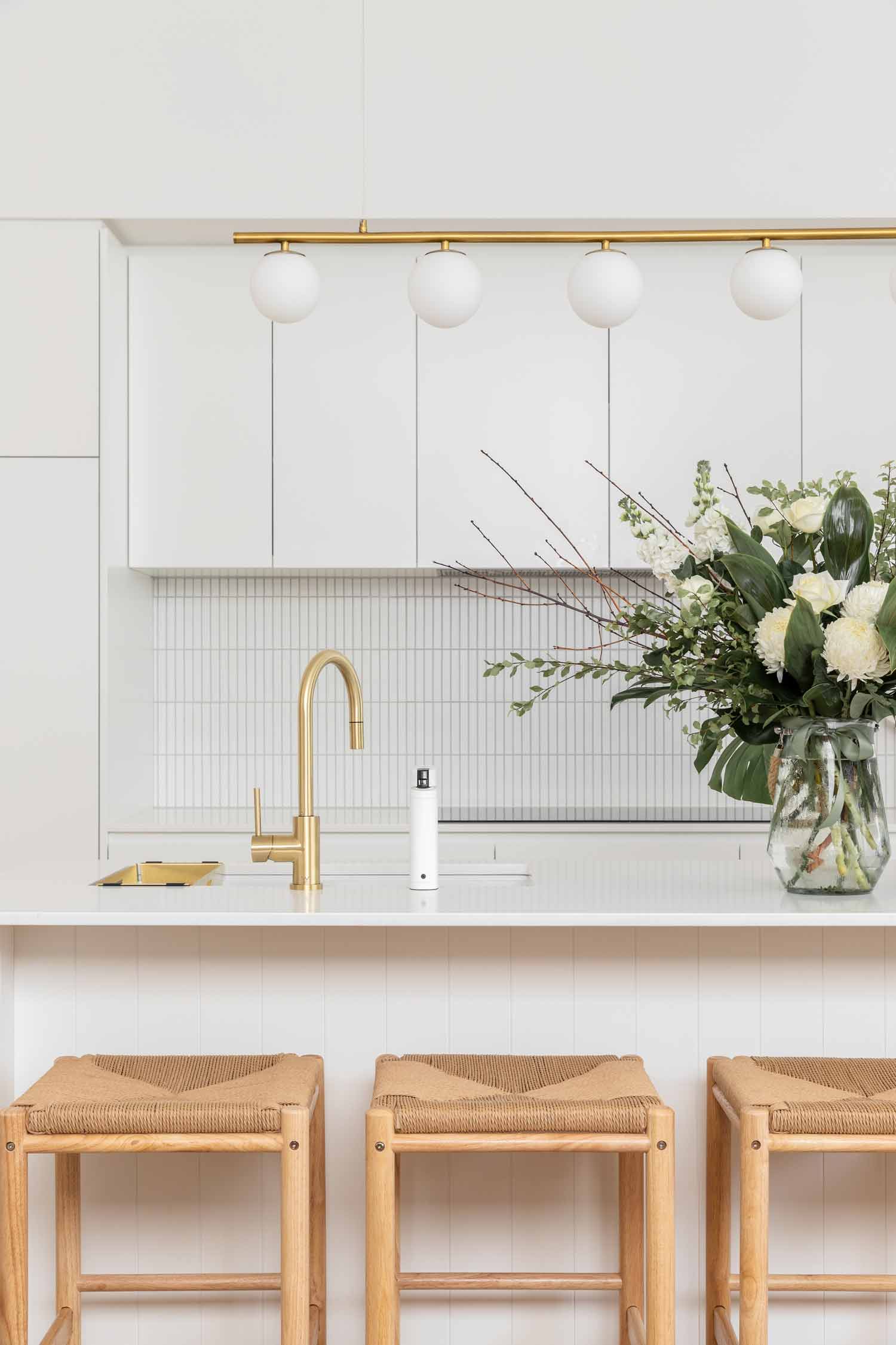 Modern-coastal-interior-design-open-plan-kitchen-with-brushed-brass-tapware-kitkat-tiles-and-timber-stools