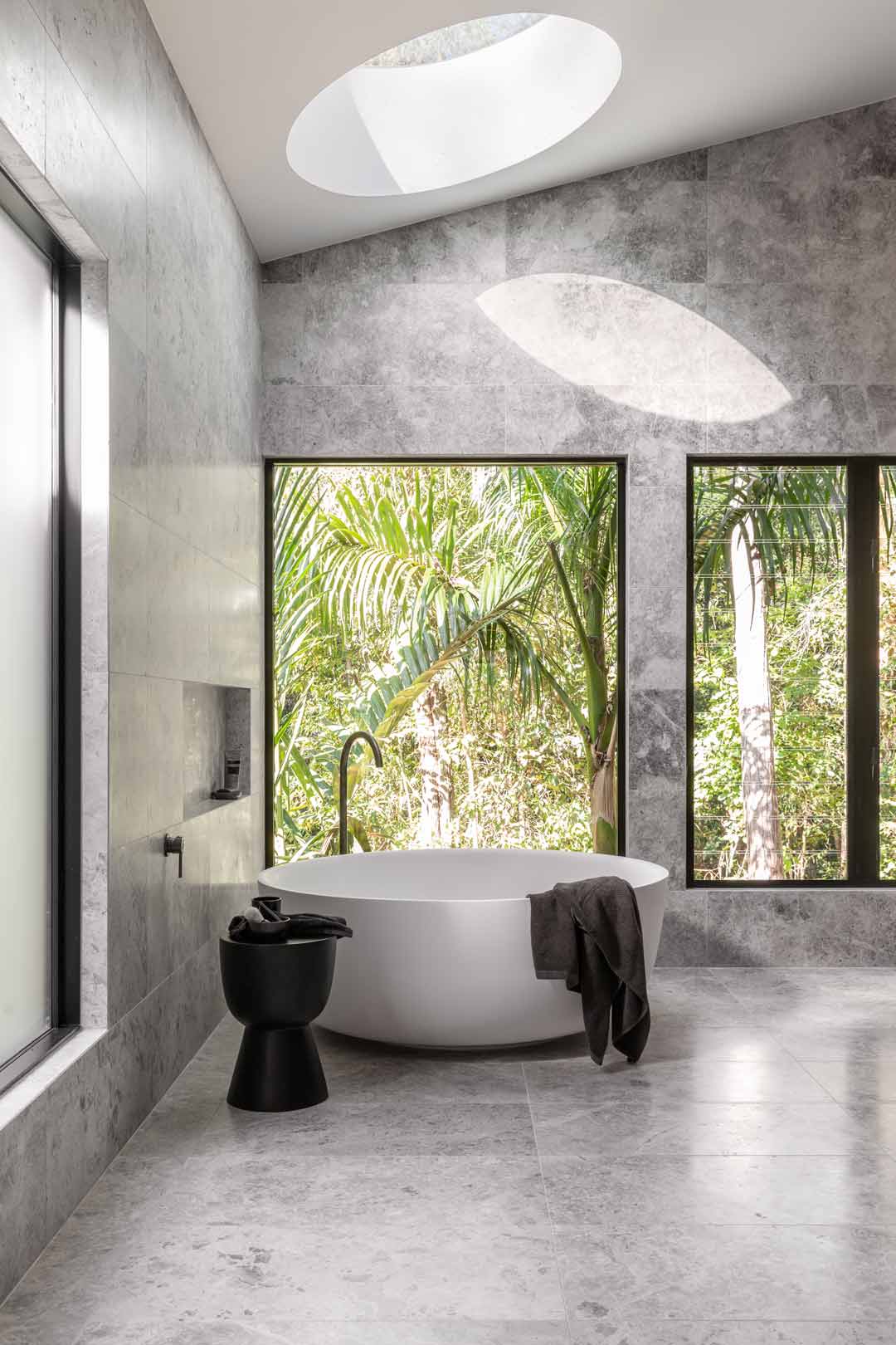 Monochromatic-ensuite-bathroom-for-Kooringal-Lodge-with-circular-bath-skylight-and-windows-letting-the-outdoors-in