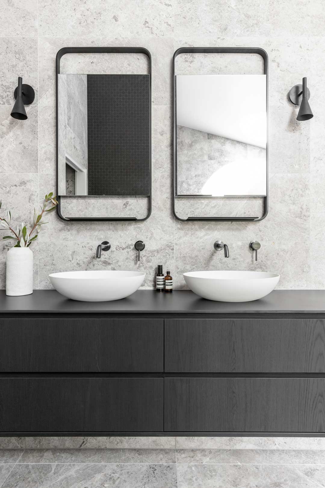 Monochromatic-industrial-style-bathroom-with-black-cabinetry-gunmetal-tapware-grey-tiles-and-symetrical-wall-sconces