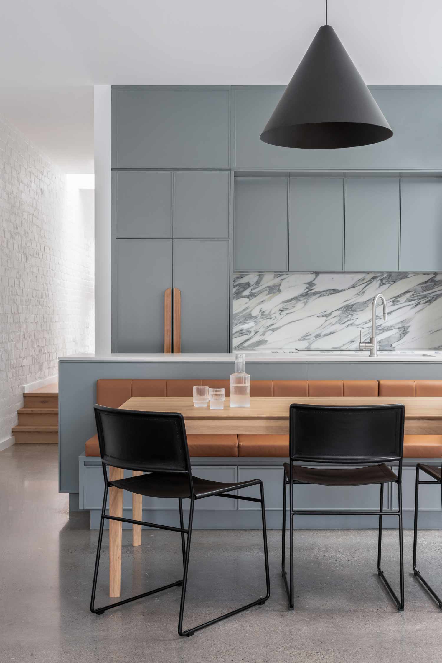 Open-plan-kitchen-in-a-modern-coastal-home-with-brushed-nickle-tapware-blue-cabinetry-timber-handles-marble-splash-back-and-a-built-in-dining-bench-1