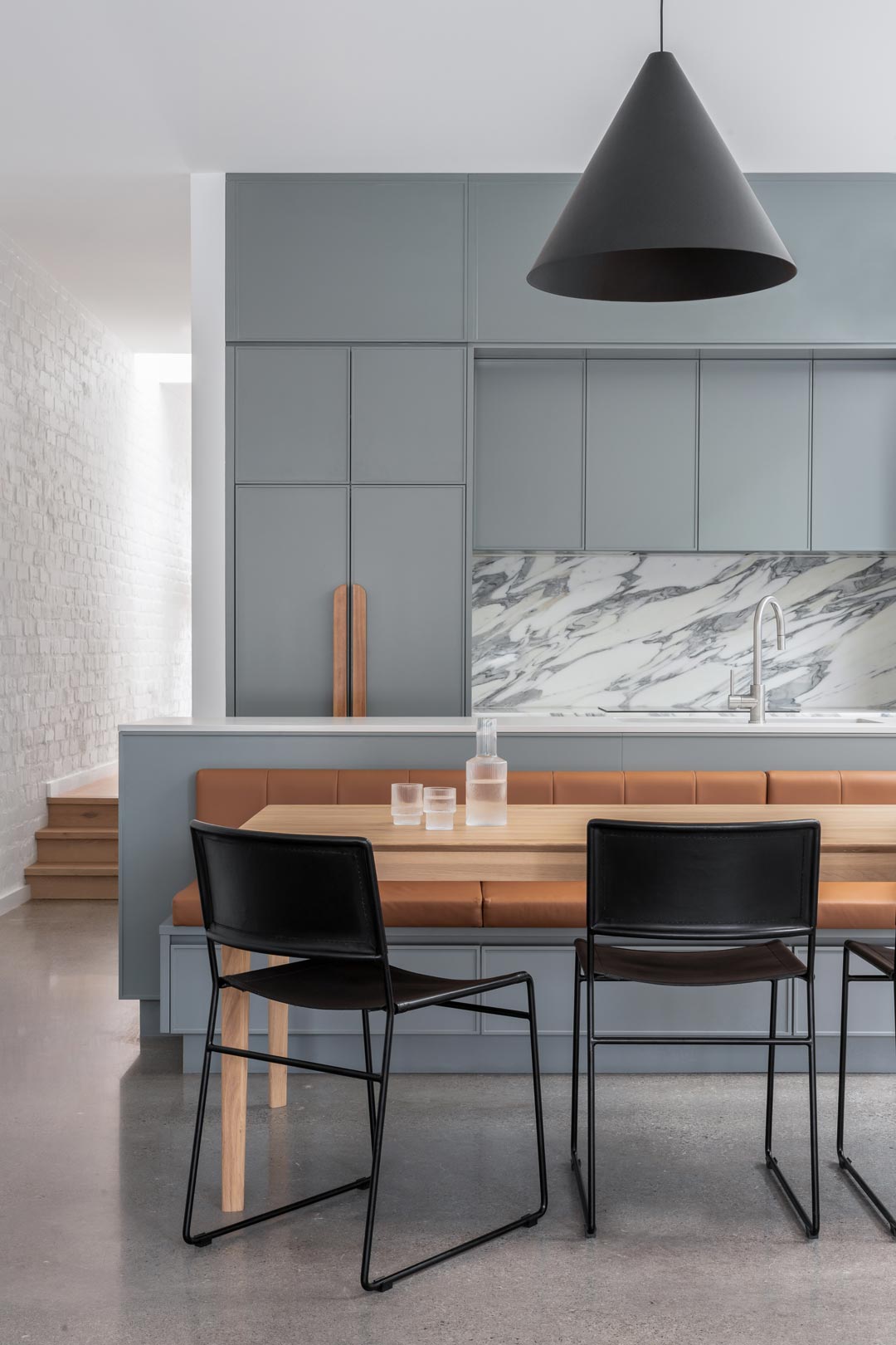 Open-plan-living-dining-space-in-a-modern-coastal-home-features-soft-concrete-floors-blue-cabinetry-stainless-steel-fixtures-and-a-marble-spash-back-1