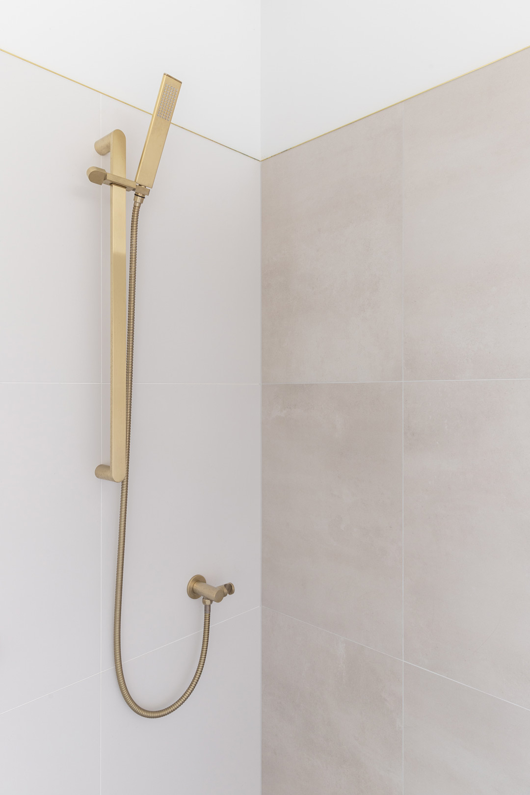 Soft-brushed-brass-hand-held-shower-set-with-neutral-tiles-in-grey-and-white